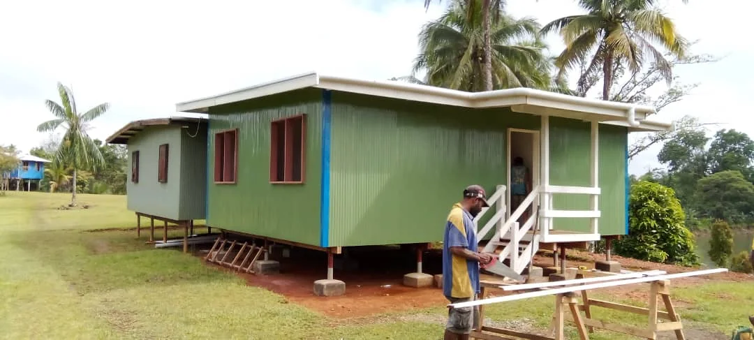 A raised community health aid post surrounded by grass and palm trees.